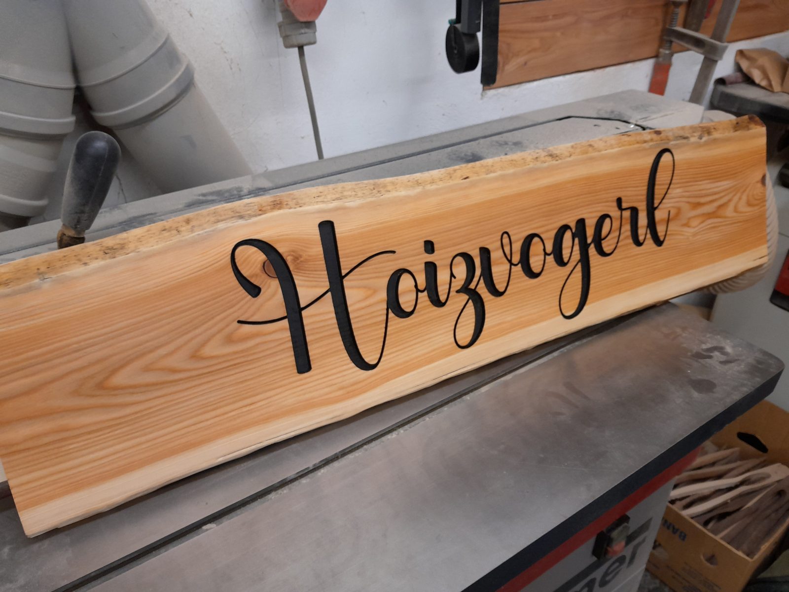 Naturbelassenes Holzschild Holzvogl mit dunkler Schrift auf langer Holzbohle